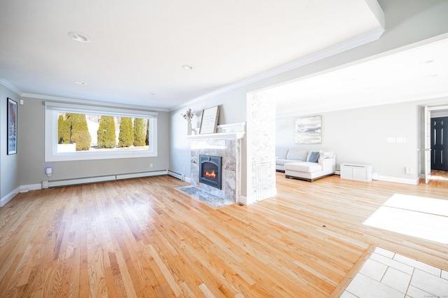 unfurnished living room with crown molding, light wood finished floors, baseboard heating, a high end fireplace, and baseboards