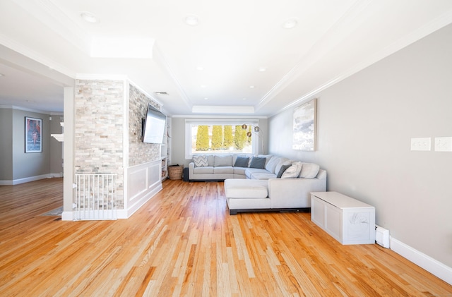 unfurnished living room with a tray ceiling, crown molding, light wood-style flooring, and baseboards