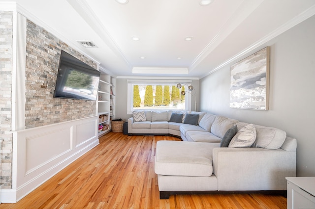 living area featuring ornamental molding, a tray ceiling, a wainscoted wall, and light wood-style flooring