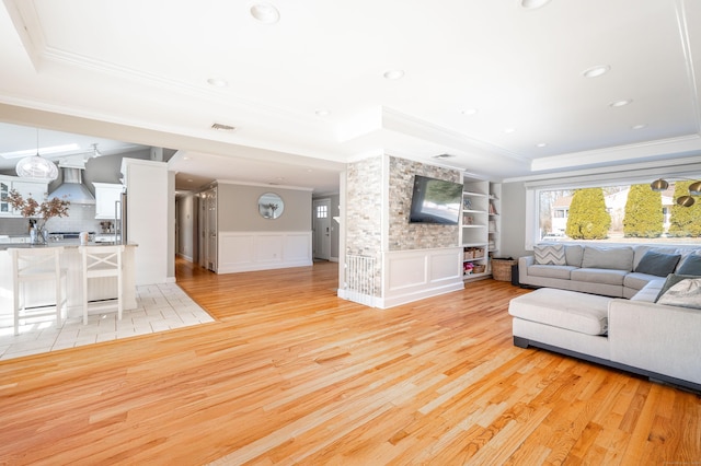 living area featuring a tray ceiling, a wainscoted wall, a decorative wall, and light wood finished floors