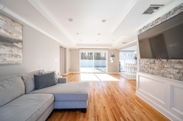 living area featuring ornamental molding, light wood-type flooring, a raised ceiling, and visible vents