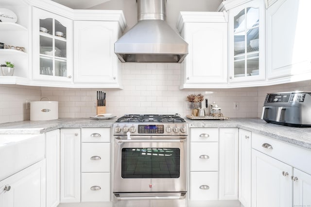 kitchen featuring wall chimney exhaust hood, backsplash, stainless steel range with gas cooktop, and white cabinets