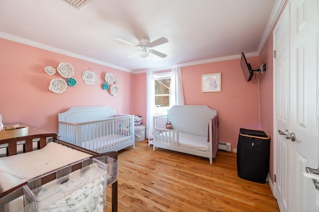 bedroom with a crib, light wood finished floors, a baseboard radiator, and ornamental molding