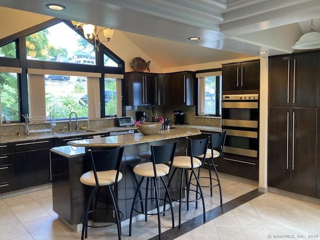 kitchen with light tile patterned floors, tasteful backsplash, a breakfast bar area, a center island, and a sink