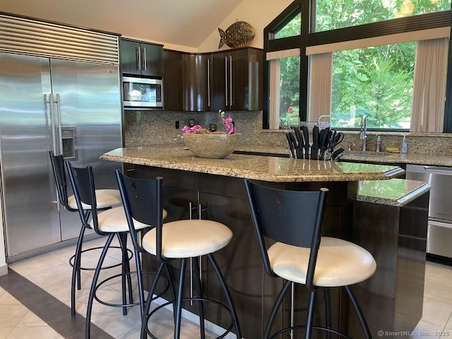 kitchen with light tile patterned floors, a center island, a sink, built in appliances, and backsplash