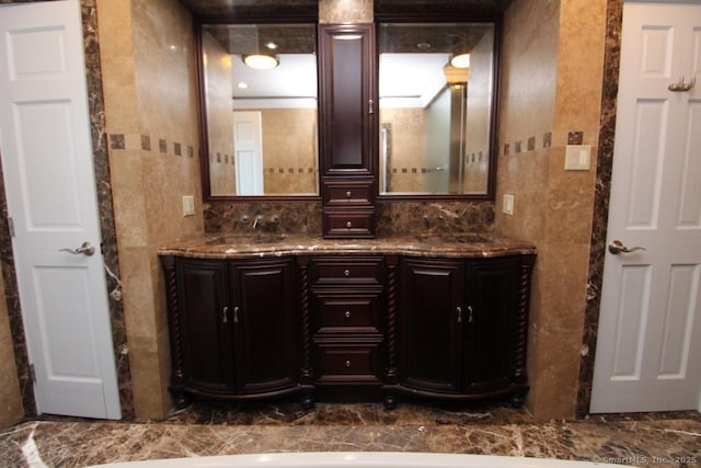 full bath featuring marble finish floor, double vanity, a sink, and tile walls