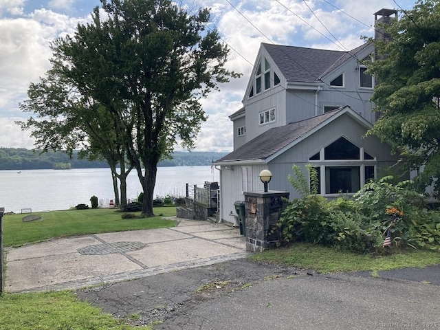 view of home's exterior featuring a shingled roof, a water view, and a yard