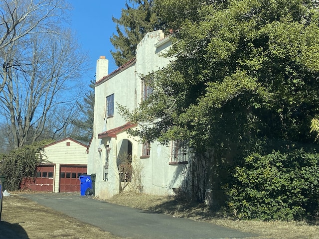 view of property exterior with a garage, a chimney, an outbuilding, and stucco siding