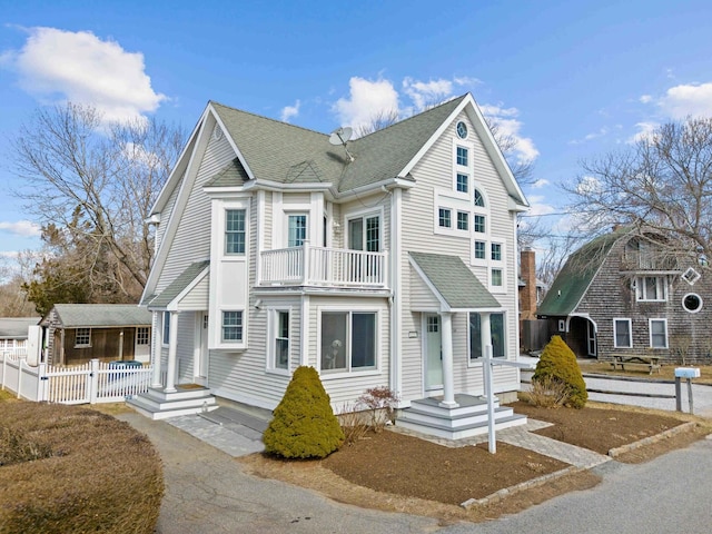 view of front of house with a porch, a balcony, fence, and a shingled roof