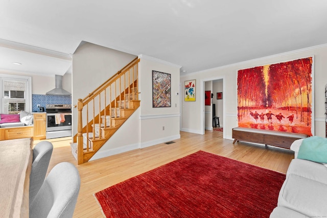 living room with visible vents, baseboards, light wood-type flooring, stairs, and ornamental molding