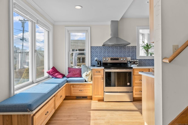 kitchen featuring light wood finished floors, light brown cabinetry, decorative backsplash, electric stove, and wall chimney range hood