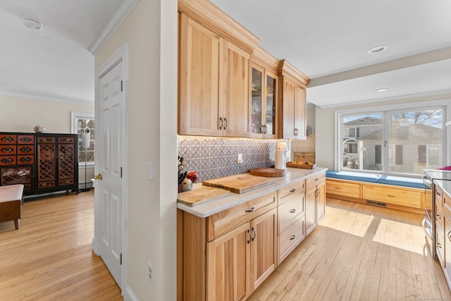 kitchen with visible vents, backsplash, glass insert cabinets, light wood-type flooring, and ornamental molding