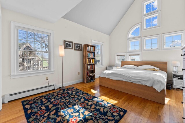 bedroom with a baseboard heating unit, baseboards, and hardwood / wood-style flooring