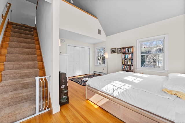 bedroom featuring visible vents, lofted ceiling, hardwood / wood-style floors, a closet, and a baseboard radiator