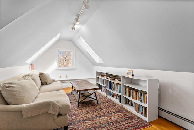 interior space with vaulted ceiling with skylight, rail lighting, wood finished floors, and a baseboard radiator