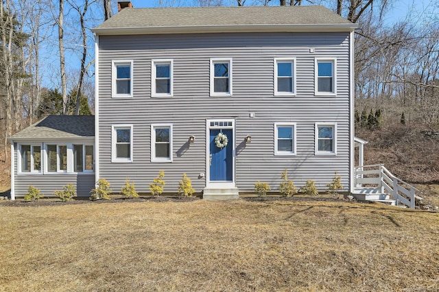 colonial-style house featuring entry steps, roof with shingles, a chimney, and a front yard