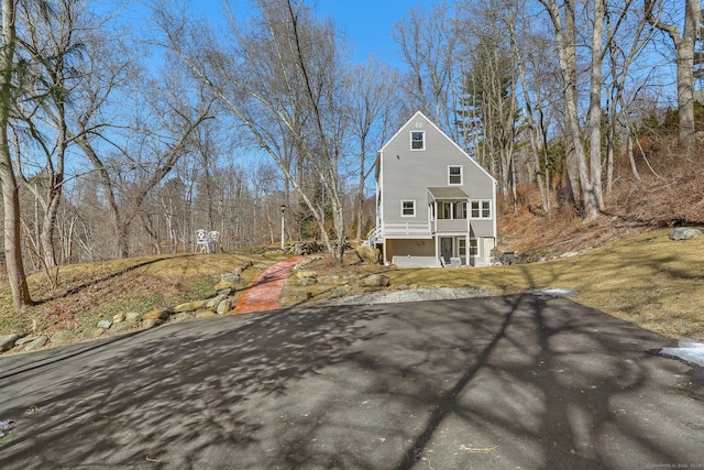 exterior space featuring aphalt driveway, a lawn, and a view of trees