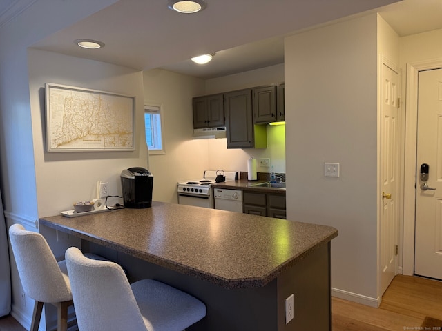 kitchen featuring a breakfast bar, dark countertops, white appliances, a peninsula, and under cabinet range hood