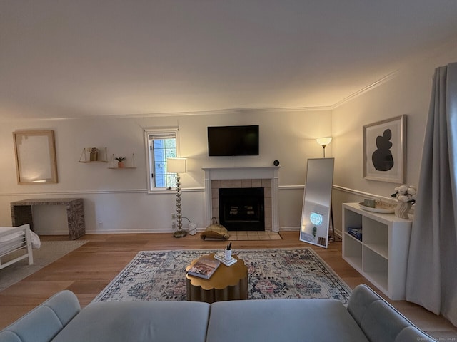 living area with crown molding, baseboards, wood finished floors, and a tile fireplace