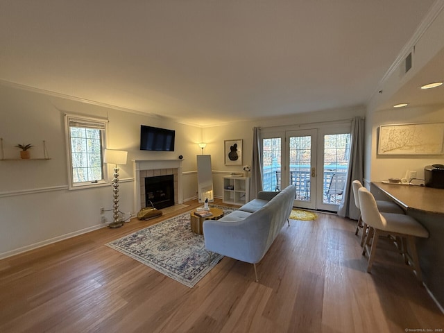 living area featuring ornamental molding, a tile fireplace, french doors, and wood finished floors