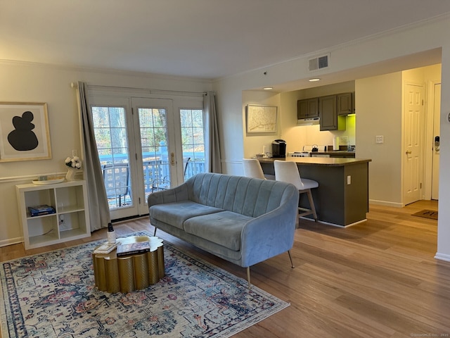 living area with light wood-type flooring, visible vents, baseboards, and crown molding