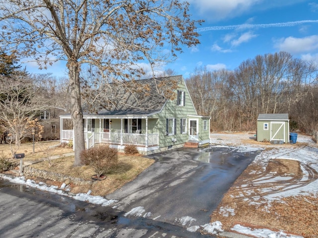 view of front of house featuring an outbuilding, a shed, aphalt driveway, and a porch