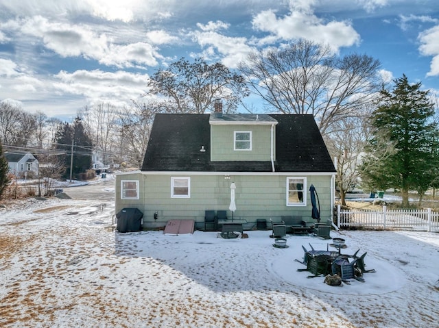 snow covered property with roof with shingles, a chimney, and fence