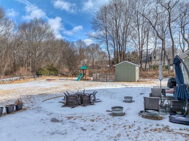 snowy yard with a playground, an outdoor structure, fence, and a storage unit