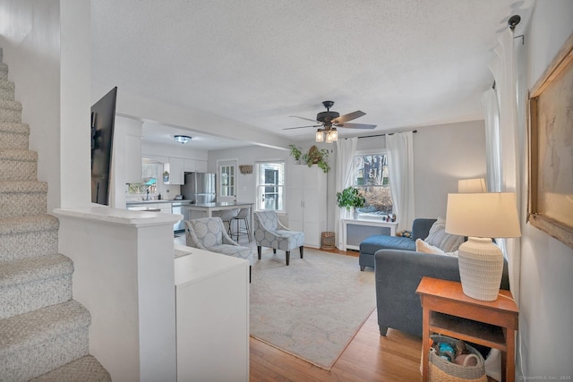 living room featuring light wood-style flooring, stairway, radiator heating unit, ceiling fan, and a textured ceiling