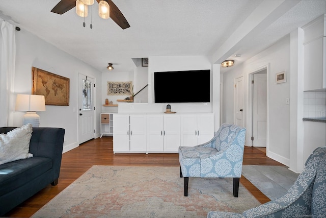 living area with ceiling fan, baseboards, dark wood finished floors, and a textured ceiling