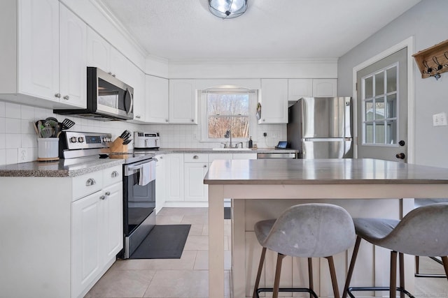 kitchen with tasteful backsplash, appliances with stainless steel finishes, white cabinets, a sink, and a kitchen breakfast bar