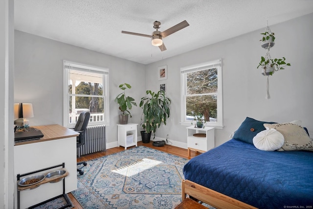 bedroom with baseboards, a ceiling fan, radiator heating unit, wood finished floors, and a textured ceiling