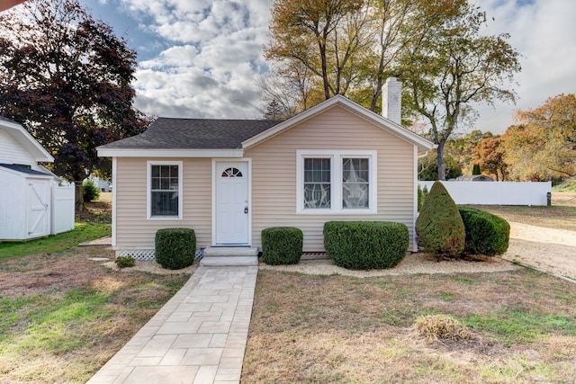 bungalow-style house with an outbuilding, a chimney, a shingled roof, a front yard, and fence