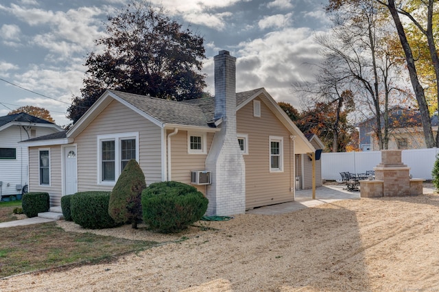 exterior space featuring a chimney, a shingled roof, a wall mounted AC, a patio area, and fence