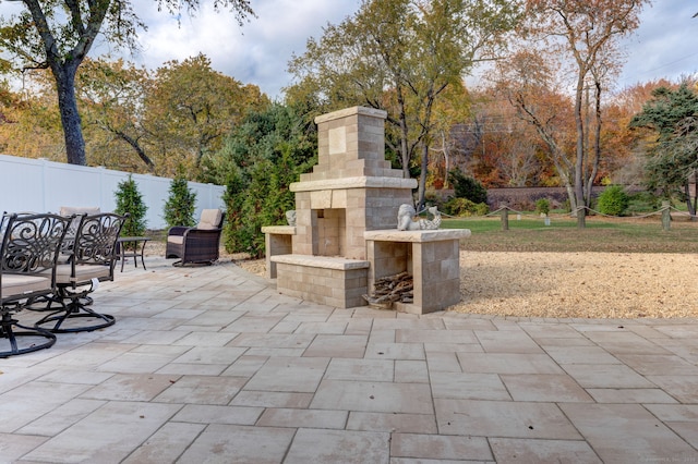 view of patio with an outdoor stone fireplace and fence