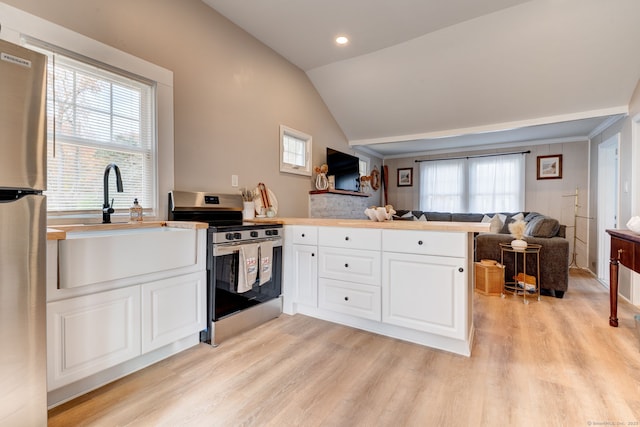 kitchen featuring appliances with stainless steel finishes, open floor plan, a sink, vaulted ceiling, and a peninsula