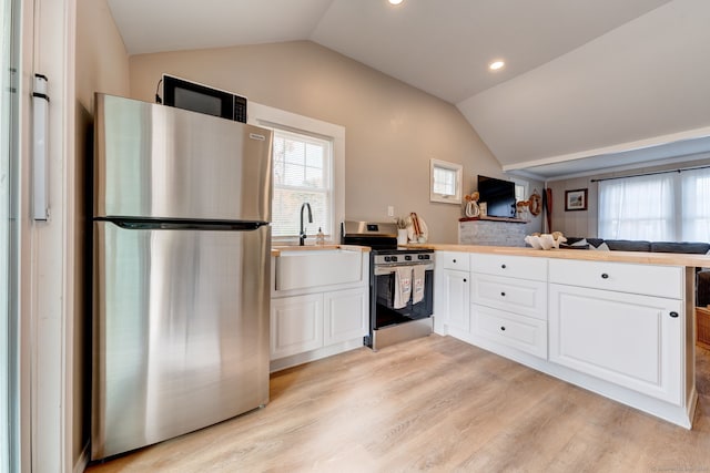 kitchen with a peninsula, appliances with stainless steel finishes, vaulted ceiling, and a sink