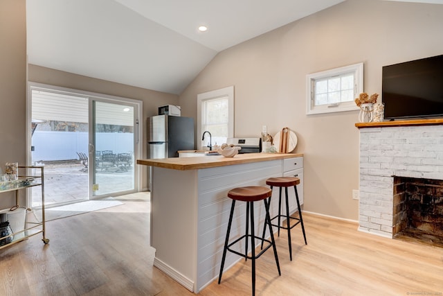 kitchen featuring lofted ceiling, butcher block counters, light wood-style flooring, freestanding refrigerator, and a kitchen breakfast bar