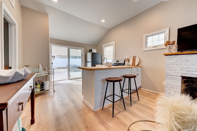 kitchen featuring lofted ceiling, a fireplace, freestanding refrigerator, and a kitchen breakfast bar