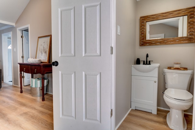 bathroom with toilet, wood finished floors, vanity, baseboards, and vaulted ceiling