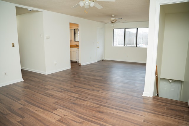 unfurnished room with dark wood-style flooring, a sink, a textured ceiling, and baseboards