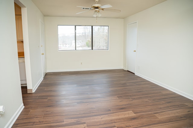 unfurnished room featuring visible vents, dark wood-type flooring, a ceiling fan, and baseboards