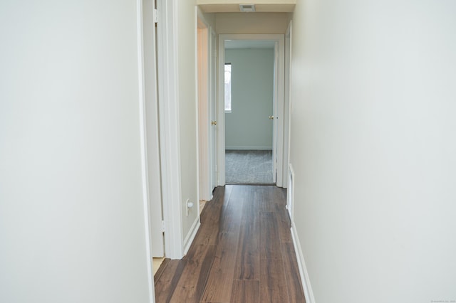 hallway with dark wood-style floors, visible vents, and baseboards