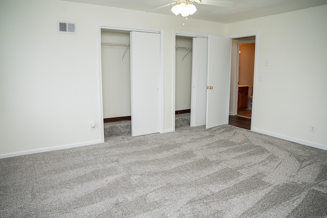 unfurnished bedroom featuring baseboards, visible vents, ceiling fan, carpet flooring, and multiple closets