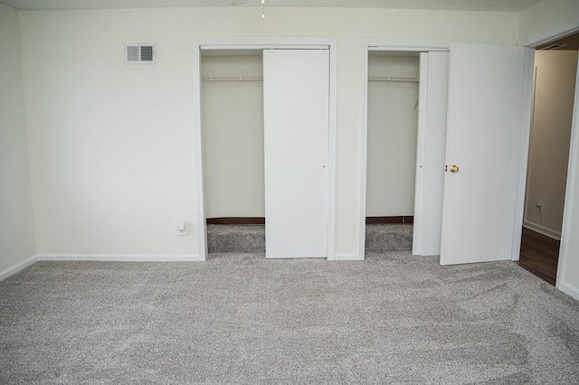 unfurnished bedroom with baseboards, carpet flooring, visible vents, and multiple closets