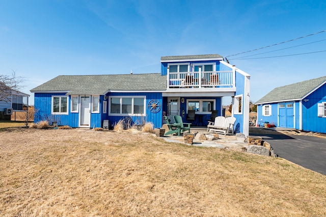 view of front of property with board and batten siding, a front yard, a balcony, and a shingled roof