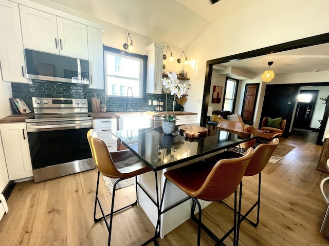 kitchen with light wood-type flooring, appliances with stainless steel finishes, white cabinets, and vaulted ceiling