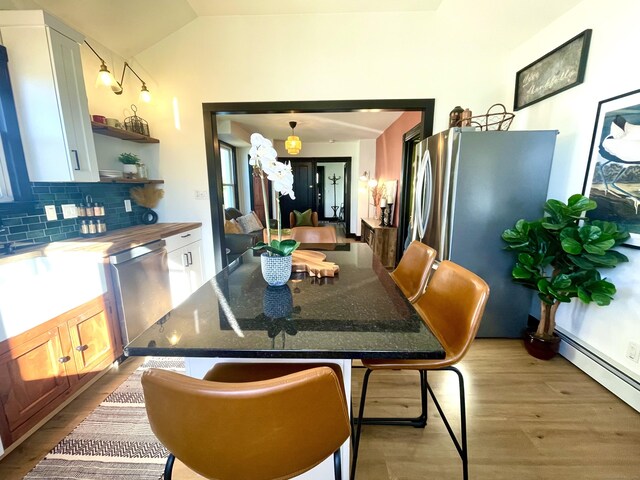 dining space featuring baseboard heating, light wood-style flooring, and vaulted ceiling