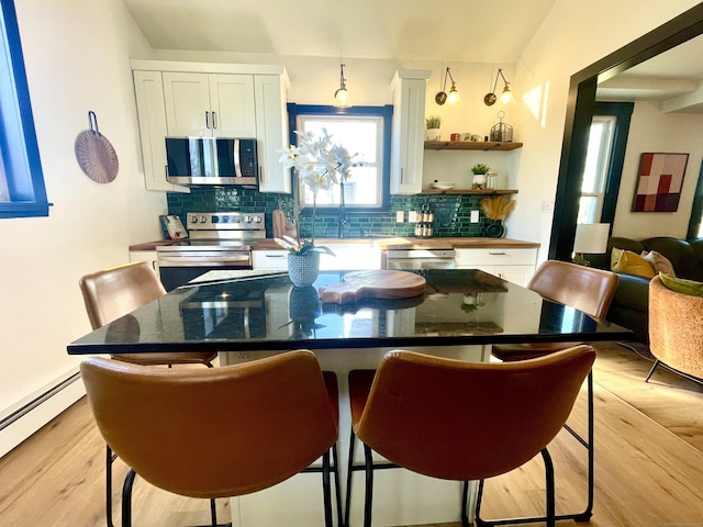 kitchen with white cabinetry, appliances with stainless steel finishes, a baseboard heating unit, light wood-type flooring, and a center island