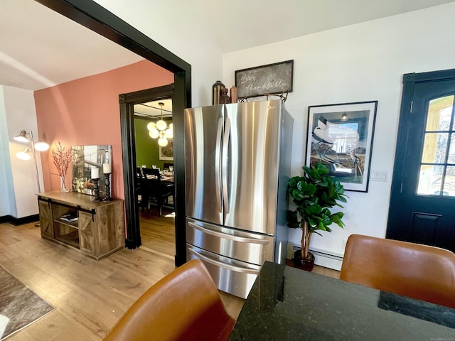 kitchen with light wood finished floors, dark stone counters, freestanding refrigerator, and a baseboard radiator